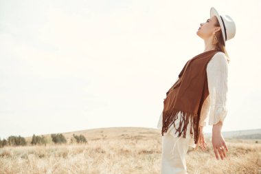 Bozkırda poz veren boho tarzı kıyafetler ve aksesuarlarla güzel bir kızın yan görüntüsü. Yaz modası. Boho ve hippi tarzı. Boşluğu kopyala.