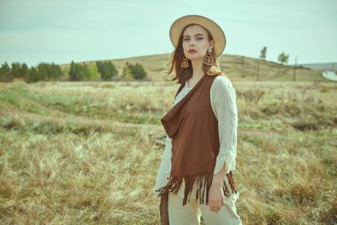 Boho tarzı kıyafetler ve aksesuarlar içinde güzel bir kız bozkırda duruyor. Yaz modası. Romantik boho ve hippi tarzı. 