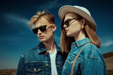 Denim tarzı. Kot pantolon ve siyah güneş gözlüğü takan, mavi gökyüzüne karşı otoyolda poz veren modaya uygun modeller. Yol seyahati otostop yapıyor. Özgürlük.