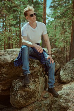 Turist yürüyüşçüsü çam ormanındaki taşların üzerinde dinlenmek için oturdu. Yürüyüş sırasında bir mola. Turizm, doğa keşfi. Yaz tatili. 