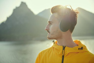 Yakışıklı bir adamın gün batımıyla tanışan, kulaklıkla hoş müzikler dinleyen, güzel bir manzaraya karşı bir dağda duran bir portresi. Seyahat, yaz tatili.. 