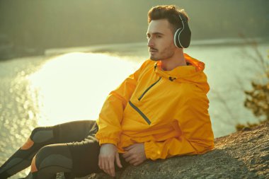 Erkek bir turist gün batımından zevk alır ve güzel bir manzaraya karşı bir dağda uzanan kulaklıkla hoş müzikler dinler. Seyahat, yaz tatilleri. Doğayla uyum..