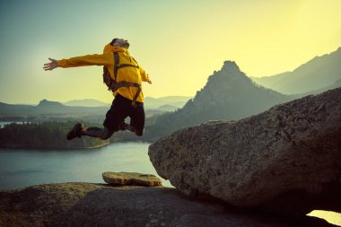 Özgürlüğü, başarıyı hissetmek. Sırtında sırt çantası olan neşeli bir turist kollarını açmış bir dağın tepesine duygusal olarak atlıyor. Aktif yaşam tarzı, yürüyüş.