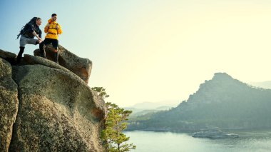 İki genç dağcının portresi bir dağın tepesinden güzel bir manzaranın tadını çıkarıyor. Olağanüstü sporlar, dağ turizmi. Özgürlüğü ve başarıyı hissetmek. Boşluğu kopyala.