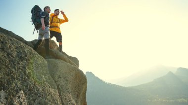 İki turist dağın tepesinde durup nefes kesici manzaranın tadını çıkarıyorlar. Olağanüstü sporlar, dağ turizmi. Özgürlüğü ve başarıyı hissetmek. Boşluğu kopyala.