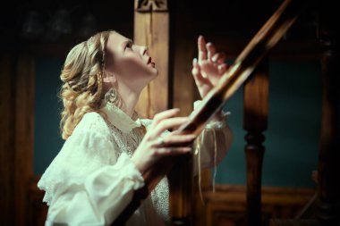 Tarihsel mistik roman. Beyaz dantelli elbiseli güzel bir bayan aristokrat eski bir şatoda merdivenlerden yukarı çıkar ve şüpheyle yukarı bakar. Viktorya tarzı.