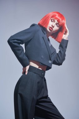 Yüksek moda. Parlak makyajlı, parlak kırmızı omuz hizasında saçlı, şık siyah takım elbiseli güzel bir bayan manken. Saç stili, saç boyası, makyaj. Gri arkaplan.