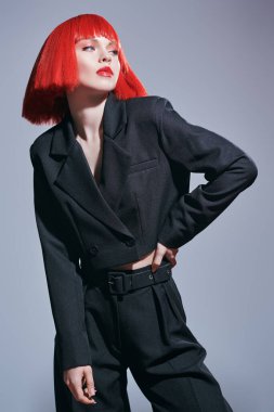 Yüksek moda. Parlak makyajlı, parlak kırmızı omuz hizasında saçlı, şık siyah takım elbiseli güzel bir bayan manken. Saç stili, saç boyası, makyaj. Gri arkaplan.