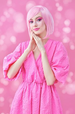 Güzellik, moda. Parlak pembe makyajlı, pembe saçlı güzel bir kızın portresi. Hayal gibi gülümseyen ve şık pembe elbiseler içinde poz veren. Işıklı pembe arkaplan. 
