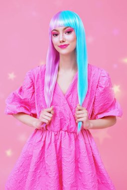 Güzel, gülümseyen bir kız mor-mavi saçlı ve pembe elbiseli sihirli yıldızlı pembe bir arka planda poz veriyor. Saç stili, saç boyası. Makyaj ve kozmetik. 