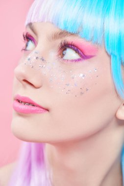 Anime makyajı. Parlak makyajlı, parlak çilli ve menekşe mavisi peruklu güzel bir kız. Pembe arka plan. Saç stili, saç boyası, makyaj. Japon animasyon tarzı. 