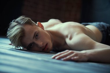 Yüzü üzüntü ve ıstırabı ifade eden çıplak bir şekilde yerde yatan genç adamın sanat portresi. Duygular, iç dünya, psikoloji. 