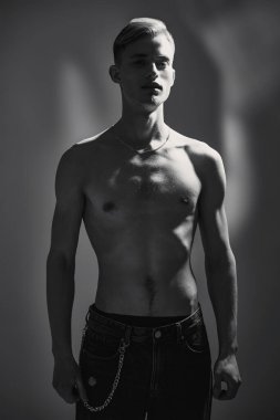 Stüdyoda karanlık ışıkta çıplak vücut pozu veren yakışıklı bir gencin siyah beyaz portresi. İnsanın güzelliği ve sağlığı. 