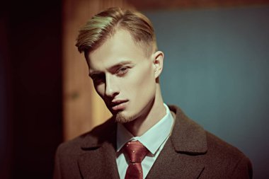 Erkek güzelliği, moda. Ciddi genç sarışın bir adam pahalı ve zarif bir ceket, beyaz gömlek ve klasik iç çamaşırı ile poz veriyor.. 