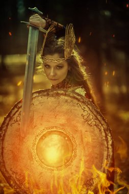 Savaşçı bir Valkyrie kadını, savaş alanında elinde bir kılıç ve kalkanla, ateşle tetikte bekliyor. İskandinav mitolojisi. Efsanevi fantezi. 