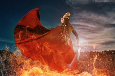 Kırmızı pelerinli ilahi kadın savaşçı Valkyrie 'nin portresi elinde bir kılıçla yanan ateşle savaşıyor. Efsanevi fantezi. İskandinav mitolojisi. 
