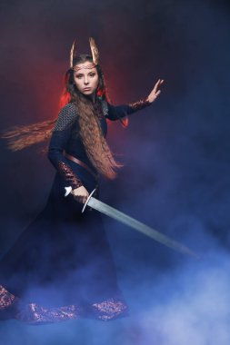 Elinde kılıçla duran ilahi kadın savaşçı Valkyrie 'nin portresi. Efsanevi fantezi. İskandinav mitolojisi. Duman ve kırmızı ışık ile koyu arkaplan.