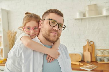 Modern bir mutfakta kızını sırtında taşıyan bir babanın portresi. Modern iç mekan, mutfak mobilyası. Mutlu aile. 