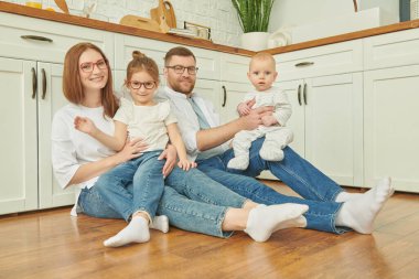 - Aile. Mutfakta yerde neşeyle oturan mutlu aile portresi. Modern iç mekan, mutfak mobilyası.. 