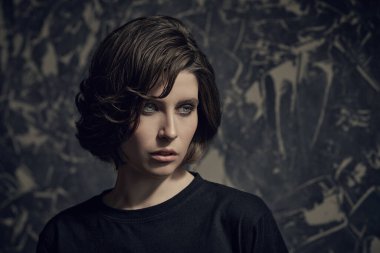 Siyah elbiseli esmer bir kız grunge duvarının arkasında duruyor ve yorgun ve ilgisiz görünüyor..