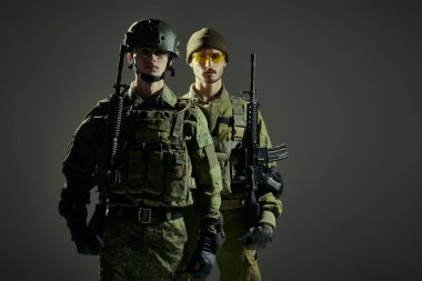 Koruyucu Muharebe Üniformalı iki asker saldırı tüfekleriyle haki bir arka planda muharebeye hazır bekliyor. Askeri bir kavram. Stüdyo çekimi.