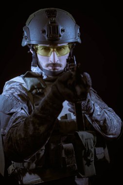 Koruyucu Savaş Üniformalı bir asker otomatik silahla kameraya bakar. Siyah arka plan. Savaş ve askeri kavram.
