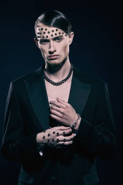 Moda konsepti. Çıplak gövdeli yakışıklı bir esmer adam siyah bir ceketle poz veriyor. Yüzünde ve elinde metal çiviler var.. 