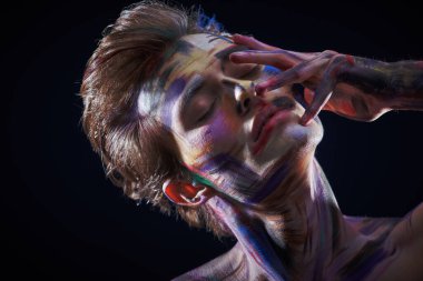 Rengarenk tenli sarışın bir adamın portresi siyah bir arka planda, gözleri kapalıyken huzur içinde duruyordu. Sanat, moda ve vücut boyası.