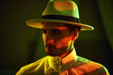 Zarif giyimli, erkeksi bir adam loş ışıkla düşünceli bir şekilde uzakta duran bir odada duruyor. Dedektif hikayesi, mafya..