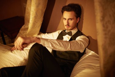 Zarif bir gece elbisesi içinde çekici bir genç adam lüks bir dairede, gece lambasında bir yatakta yatıyor. Göz kamaştırıcı bir yaşam tarzı. Erkek modası.