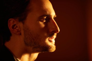 Siyah ışıklı bir odada duran yakışıklı bir esmer adamın portresi. Erkek güzeli, moda. Kara film stili.