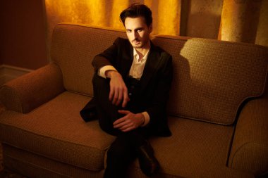 Lüks bir dairede kanepede oturan zarif giyimli, yakışıklı bir esmer adamın portresi. Göz kamaştırıcı bir yaşam tarzı. Moda fotoğrafı.. 