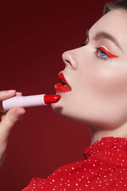 Güzellik kızı. Sevimli kırmızı renk. Parlak makyajlı güzel bir kız modelinin portresi muhteşem bir kırmızı ruj tutar. Burgundy arkaplanı.
