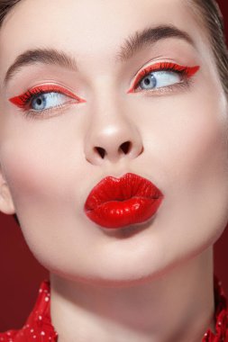 Kozmetik ve makyaj malzemeleri. Parlak kırmızı rujlu ve gözlerinde kırmızı oklar olan sevimli sarışın bir kız dudaklarını büyüleyici bir şekilde büzüyor. Güzellik konsepti.