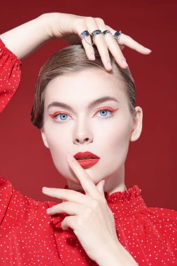 Parlak kırmızı okları ve kırmızı bir arka planda poz veren kırmızı bir bluzu olan zarif bir kadının portresi. Makyaj ve kıyafetlerde kırmızı renk. 