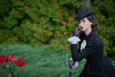 19. yüzyılın siyah takım elbiseli ve şık şapkalı güzel bir bayan parkta yürüyor.. 