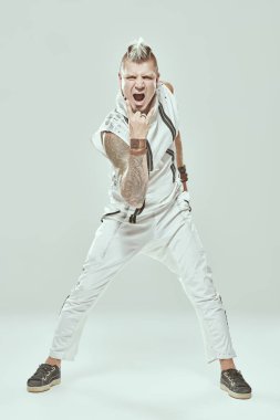 Beyaz tulumlu havalı bir punk rock müzisyeni hafif bir stüdyoda poz veriyor ve çığlık atıyor. Siber punk stili. 