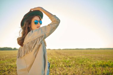 Modern batı tarzı elbiseli güzel kız güneşli bir günde sonbahar kırsalının arka planında poz veriyor. Moda fotoğrafı. Boşluğu kopyala.