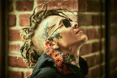 Kafasında ve boynunda etnik dövmeler ve punk stili Mohawk rastaları olan olgun, vahşi bir adamın portresi. Serseri ve rock kültürü. 