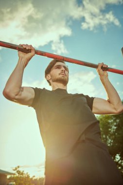 Sportif genç adam gün batımında parktaki yatay bir barda barfiks çekiyor. Spor açık havada. Aktif ve sağlıklı yaşam tarzı.