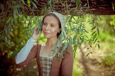 18. yüzyılın İskoç elbiseli şirin bir ortaçağ kızı yaz ormanlarında huzur içinde yürüyor. 18. yüzyılın tarihi yeniden yapılandırması. İskoç kız.