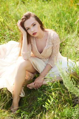 Güzel dantel elbiseli muhteşem bir kız güneşli bir günde yeşil çimlerin üzerinde oturur. Yaz özgürlüğü. Güzellik ve moda. 