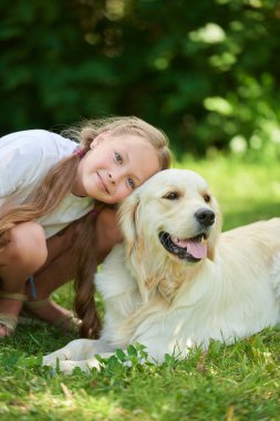 Bir yaz parkında yeşil çimlerin üzerinde köpeğiyle oynayan mutlu bir kızın portresi. Yaz tatili. Parkta dinlen..