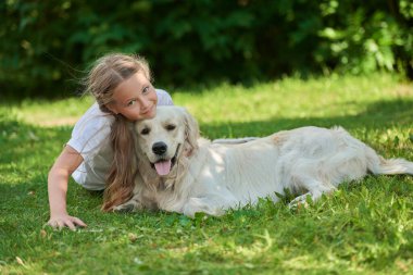 Mutlu yaz günleri. Mutlu bir kızın portresi yeşil çimlerin üzerinde köpeğiyle birlikte bir yaz parkında neşeyle yatıyor. Yaz tatili. Parkta dinlen..