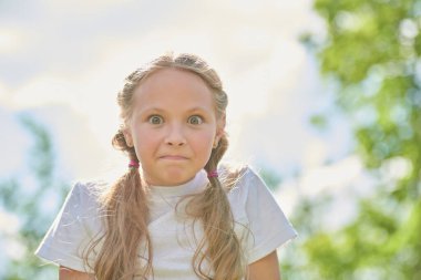 Mutlu yaz zamanları. Güneşli bir yaz gününde saçı örgülü şirin ve komik bir kızın portresi. Şaşkınlıkla kameraya bakıp gülümsüyor. Yaz tatili.