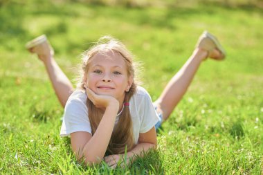 Mutlu yaz tatilleri. Bir yaz parkında yeşil çimlerin üzerinde neşeyle uzanan günlük kıyafetlerle güzel bir kızın portresi..