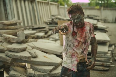 Zombi saldırıları. Kızgın kanlı zombi adam kollarını yıkılmış şehirde duran kurbana doğru uzatıyor. Cadılar Bayramı. Korku filmi. Zombi Kıyameti.