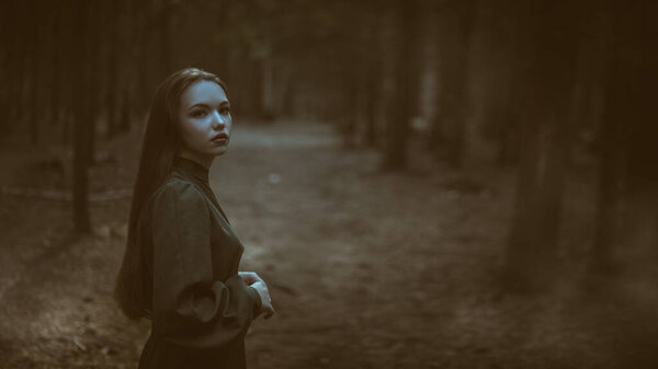 Милая сказочная девушка в длинном зеленом платье бродит в темном густом лесу. Фантазия, героиня сказки. Копирование пространства.