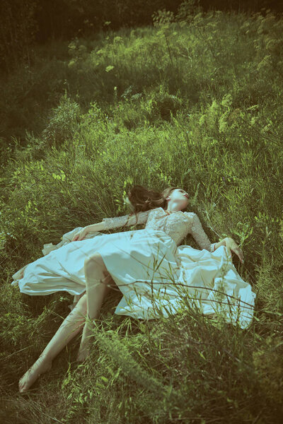 Красивая девушка, одетая в роскошное кружевное платье лежит на зеленой траве в природе. Летняя красота и мода.