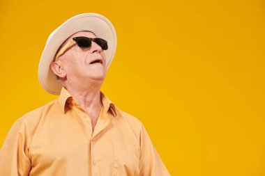 Yazlık giysiler ve güneş gözlüğü takan zarif bir adamın portresi neşeyle yukarı bakıyor. Fotokopi alanı olan sarı stüdyo. Emeklilik yaşı. Yaşlılar için yaz tatili.